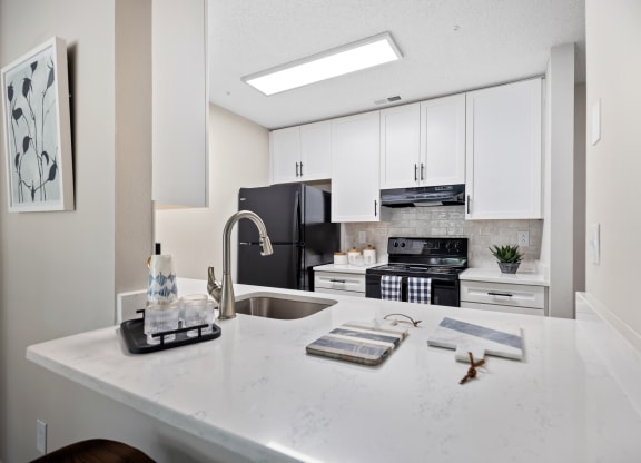 an open kitchen with white cabinets and a white counter top with a sink and stove