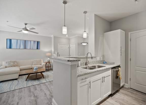 A modern kitchen with a white color scheme and a living room area with a sofa and a table.