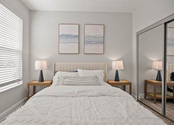A bedroom with a large bed, two lamps, and two framed pictures on the wall.