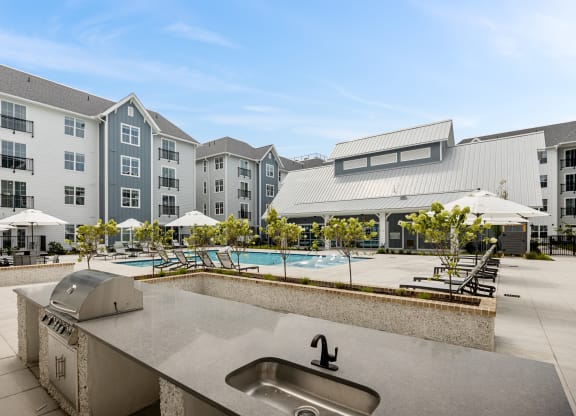 an outdoor kitchen with a sink and a pool in front of an apartment buildingat Oak Grove at Blake Farm, Wilmington, North Carolina