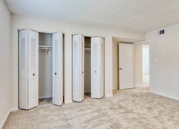 A room with white walls and a carpeted floor with four white closets.
