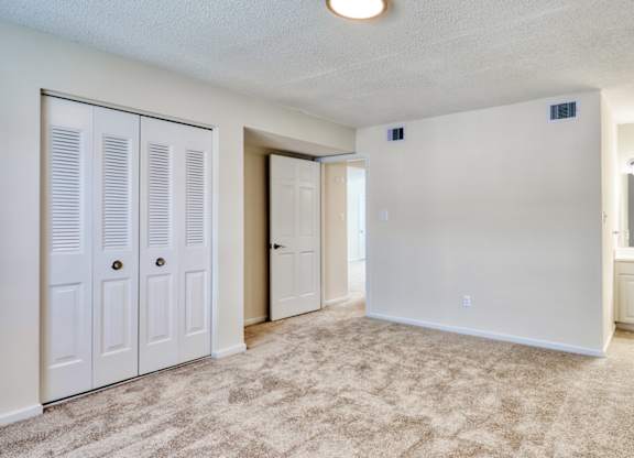 A room with white walls, a carpeted floor, and a small window with blinds.
