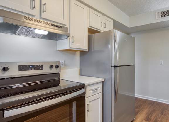 A kitchen with a stove top oven, refrigerator, and wooden floors.