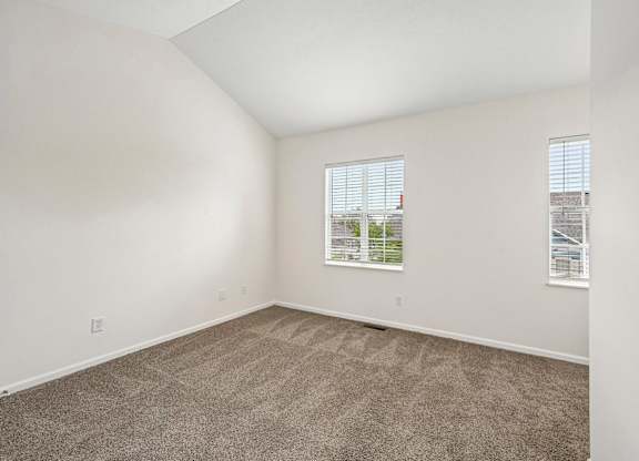 A room with carpeted floor and two windows.