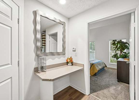 A white door is on the left of a room with a mirror and a bed in the background.