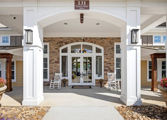 the front entrance of a building with white columns and a large archway with chairs