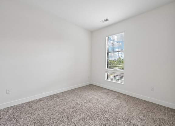 A room with a carpeted floor and a window with blinds.