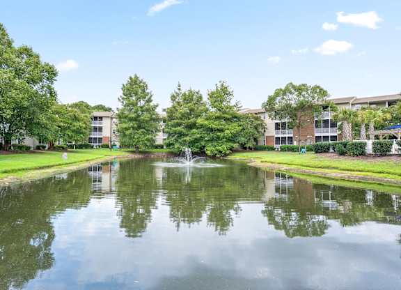 A serene pond in the middle of a park with buildings in the background at Litchfield Oaks Apartments in SC, 29585
