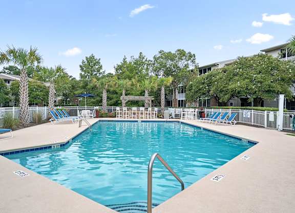 A large swimming pool surrounded by palm trees and lounge chairs at Litchfield Oaks Apartments in Pawleys Island, 29585