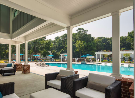 a covered patio with couches and chairs and a pool in the background