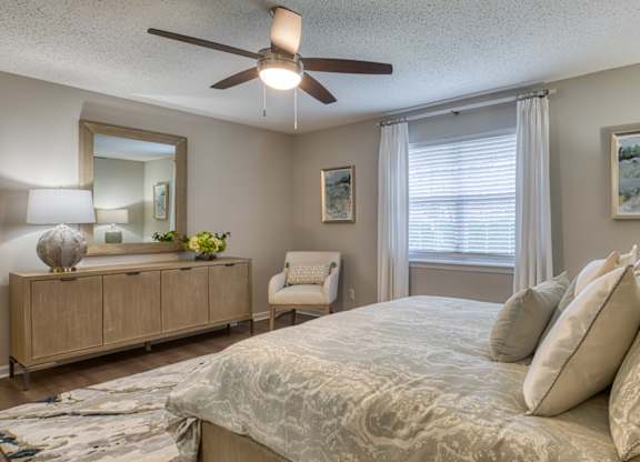 A bedroom with a large bed, a ceiling fan, and a chair.