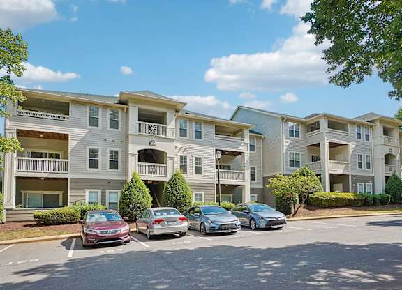A row of apartment buildings with cars parked in front.