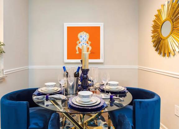 A dining table set with blue chairs and a gold sunburst mirror.