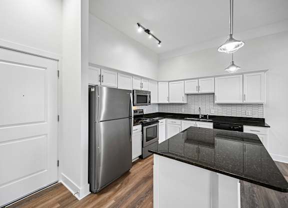 A modern kitchen with a stainless steel refrigerator and black countertops.