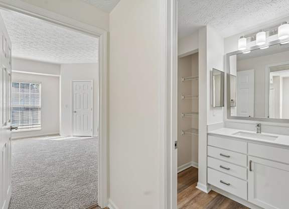 A white bathroom with a sink, mirror, and wooden floors.