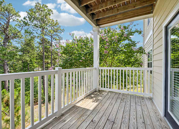 A wooden deck with a white railing and a view of trees.