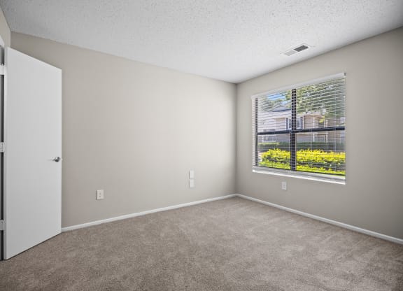 an empty bedroom with a large window and carpeted flooring
