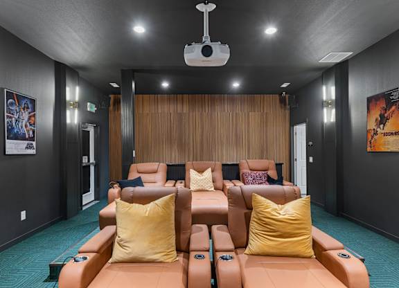 A home theater with a row of reclining seats and a projector hanging from the ceiling.