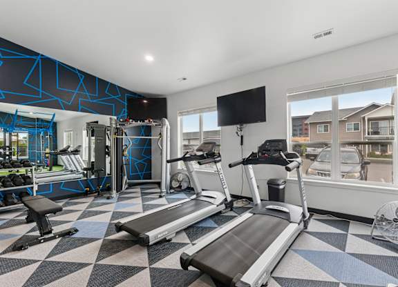 A treadmill and a bench are in a gym with a window showing a residential area.
