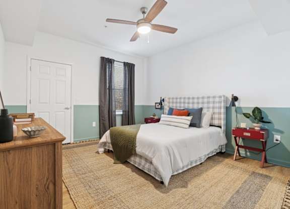 A bedroom with a bed, nightstand, and a fan.
