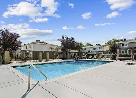 A swimming pool surrounded by a concrete patio and a fence.