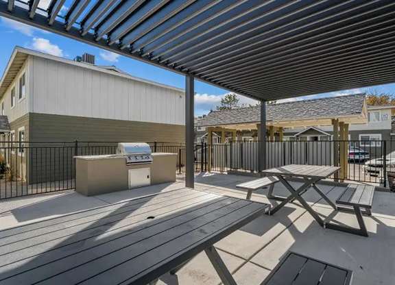 A patio area with a grill and picnic tables.