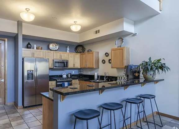 A kitchen with a refrigerator, stove, and bar stools.