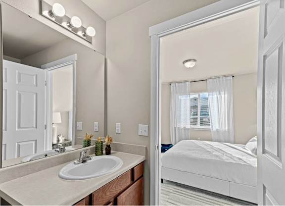 A white bathroom with a sink, mirror, and bed.