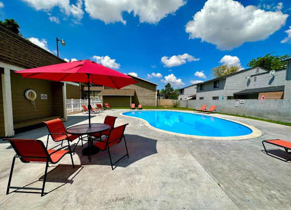 A pool area with a table and chairs and a red umbrella.