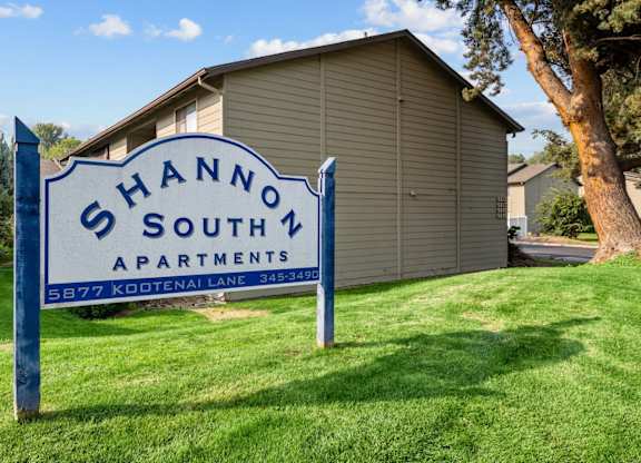A blue and white sign that says Shannon South Apartments stands in the grass in front of a building.