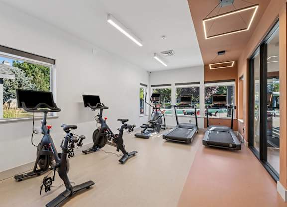 A gym with exercise equipment and a window showing a view of trees and a building.