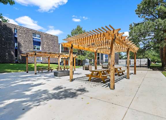 A wooden pavilion with benches is situated in a courtyard.