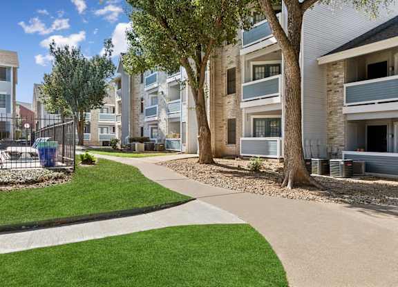 Curved walkway through landscaped courtyard with mature trees at Polo Club Apartments, Austin, TX