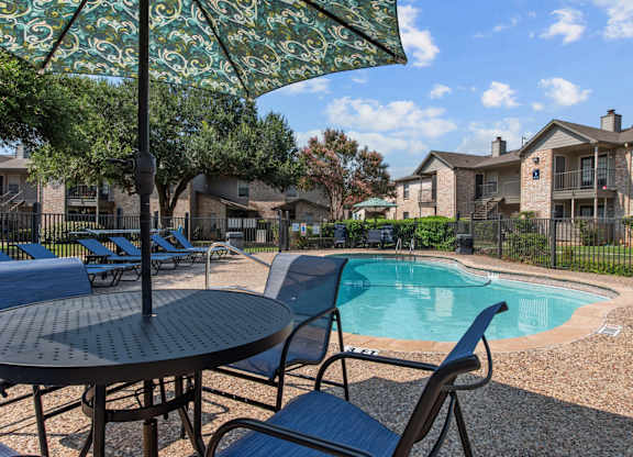 Pool area with patio furniture and decorative umbrella at Peaks at Universal City Apartments, Universal City, Texas