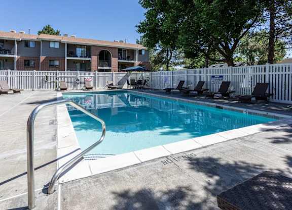A pool surrounded by a white fence and chairs.