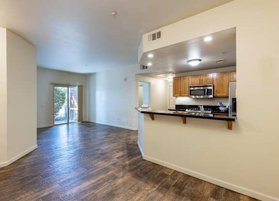 A spacious living room with hardwood floors and a kitchenette in the background.