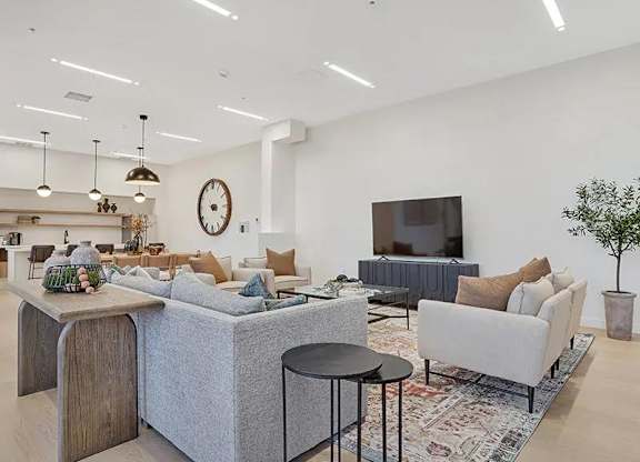 A modern living room with a grey sofa, a wooden table, and a large clock on the wall.