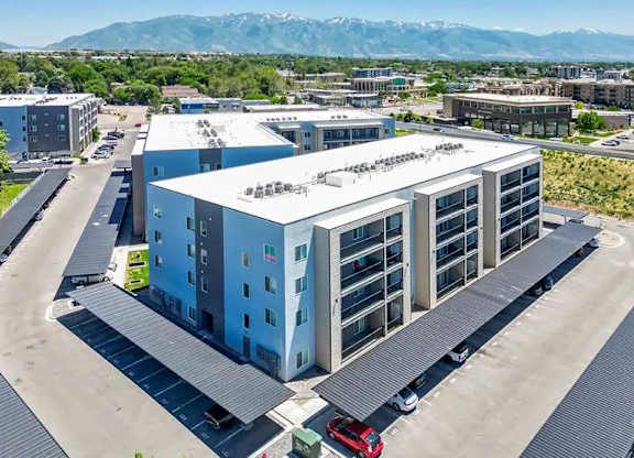A large modern building with a parking lot in front and mountains in the background.