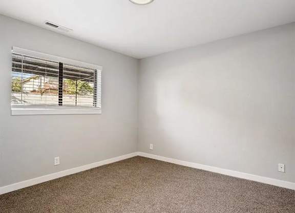 A room with a carpeted floor and a window with blinds.
