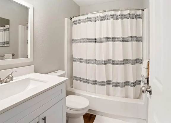 A white bathroom with a toilet, sink, and shower curtain.