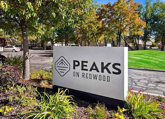 A sign that says Peaks on Redwood in front of some trees.