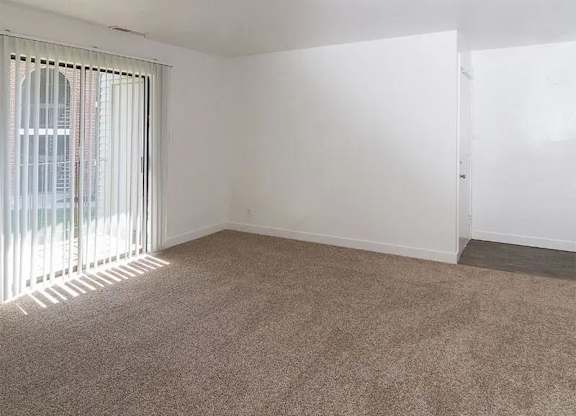 A room with a carpeted floor and a window with blinds.