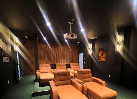 A row of orange chairs are lined up in a dark room with green carpeting.