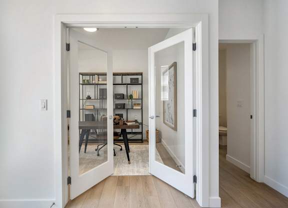 A white door opens to a room with a desk and chairs.