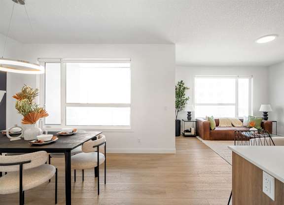 A modern dining room with a table set for two and a couch in the background.