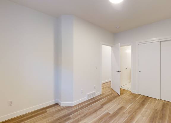 A room with white walls and wooden flooring with a door on the right.