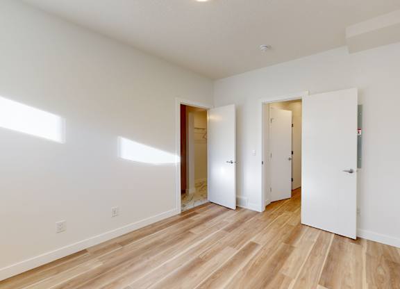 A room with white walls and wooden flooring with three doors.