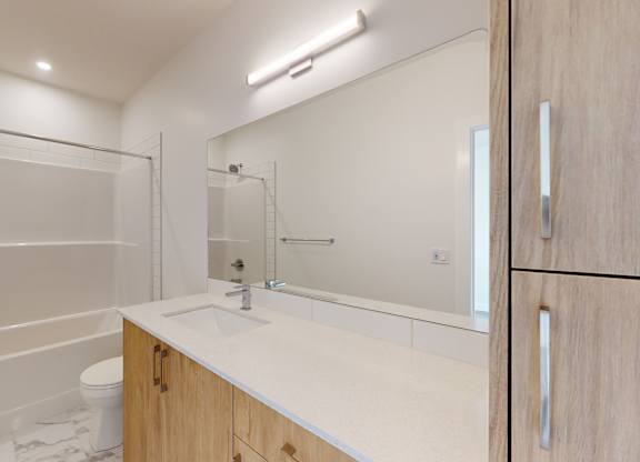 A white bathroom with a wooden vanity and a glass shower stall.