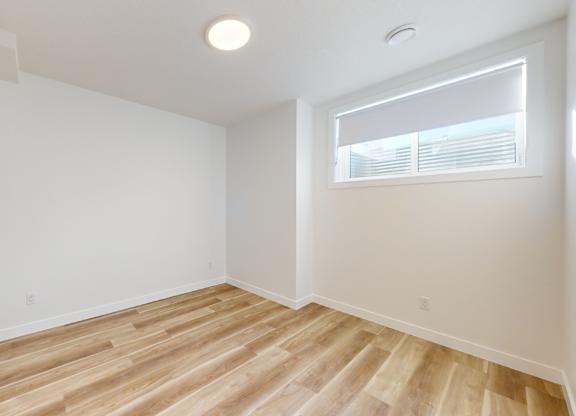 A room with wooden flooring and a window with blinds.