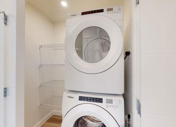 A white washing machine is stacked on top of another white washing machine in a small laundry room.